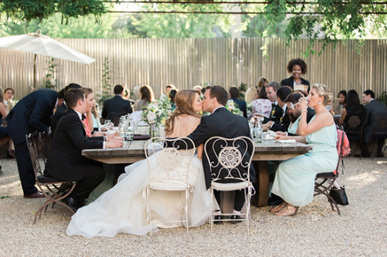 Bride and groom kiss at rustic outdoor wedding reception