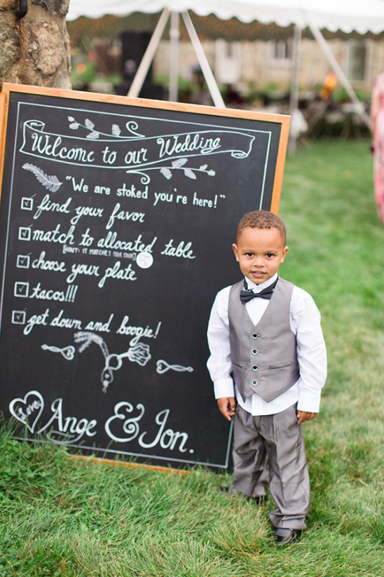 Cute ring bearer poses by wedding welcome chalkboard