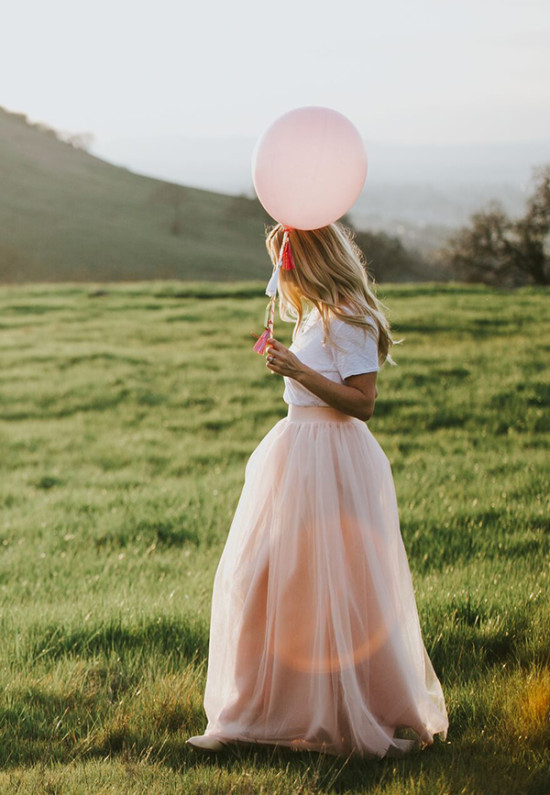 Woman with a pink balloon stands in a green field, sunny day
