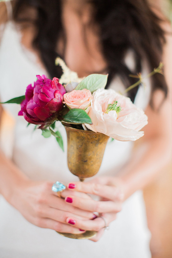 Bride holding small gold vase with pink and red flowers