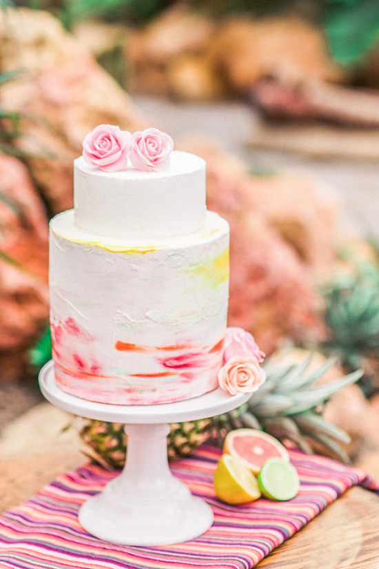 Two-tiered cake with flowers, fruits, and a vibrant watercolor design
