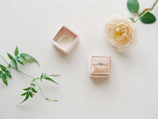 Elegant engagement ring in pink box next to a pale rose