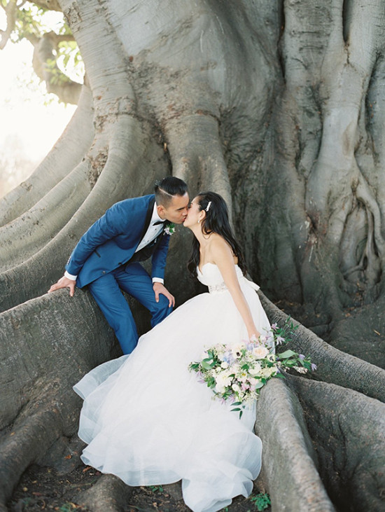 Bride and groom share a kiss by the old tree roots