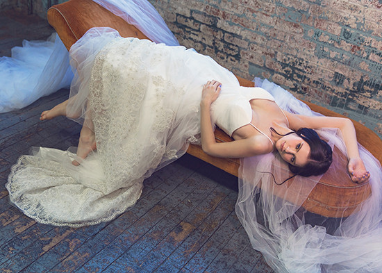 Elegant bride in lace dress poses lying on rustic bench