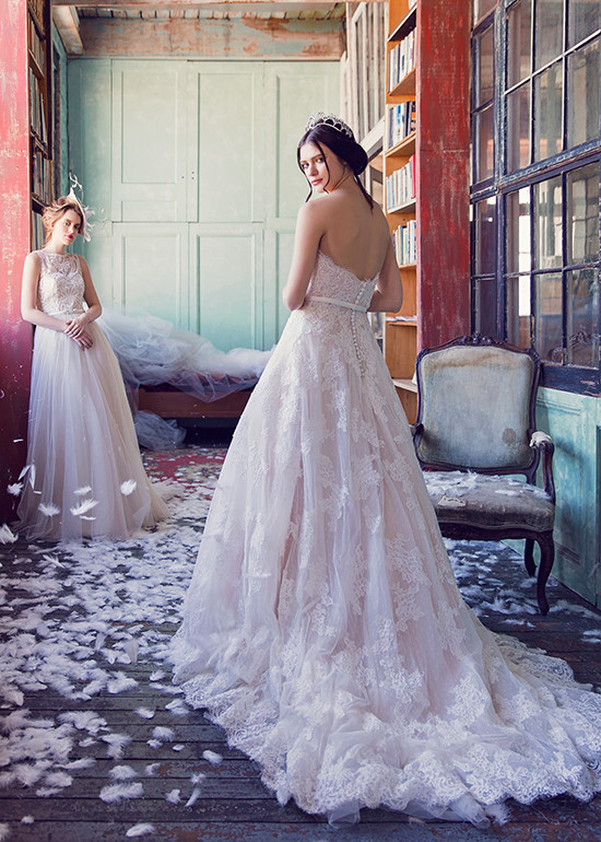 Bride in strapless lace gown looks back amid feathers room