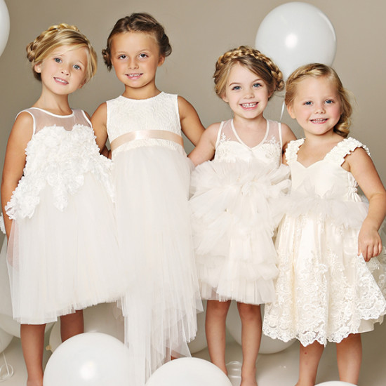 Four adorable flower girls in white dresses smiling happily