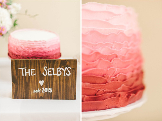 Wedding cake with pink ombre frosting next to a wooden sign