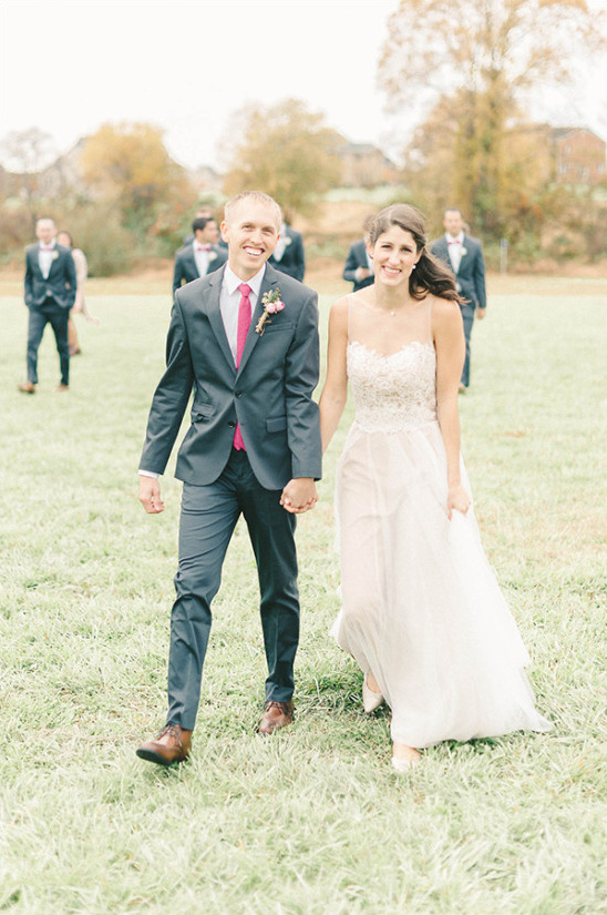 Newlywed couple walking hand-in-hand across a grassy field together