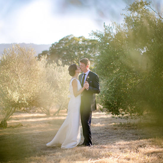 Newlyweds share a kiss in a sun-drenched outdoor wedding