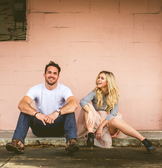 Smiling couple sitting in front of a pink wall, looking happy