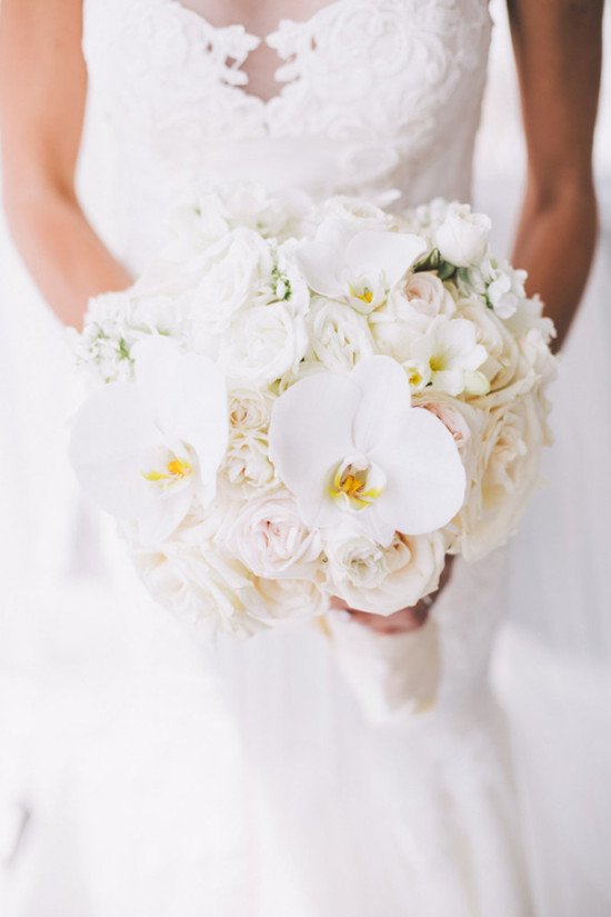 Bride holding a white elegant wedding bouquet with orchids and roses
