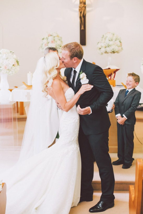 Newlyweds share a kiss at the altar, witnessed by a happy boy