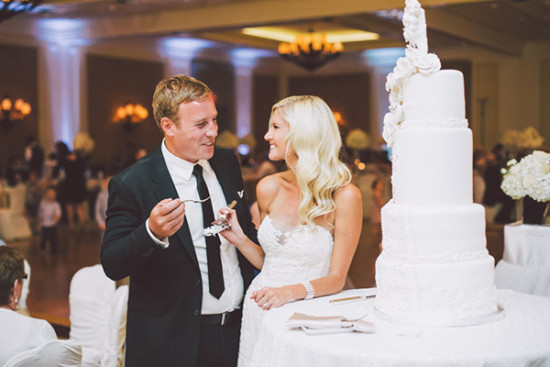 Bride and groom share cake at wedding reception, elegant white cake