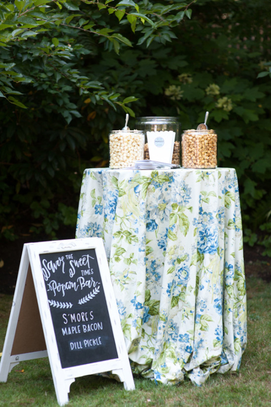 Popcorn bar with a floral tablecloth and menu in an outdoor event