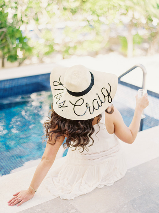 Woman with custom Craig hat by pool, holding a drink, ready for fun