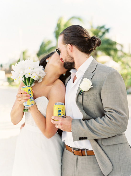 Newlyweds share a kiss and Pacifico beers at a beach wedding