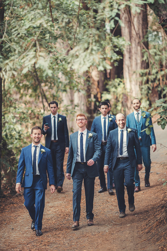 Groomsmen in suits walking down a path surrounded by trees