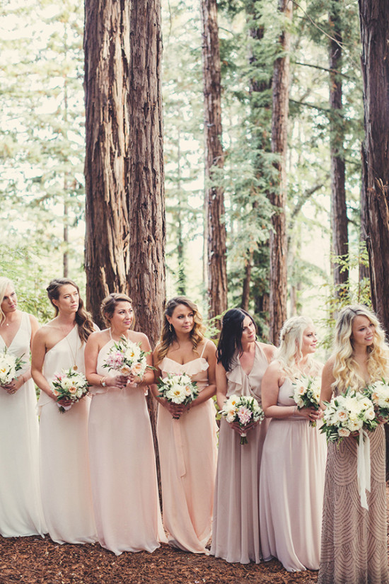 Bridesmaids in blush dresses holding bouquets during outdoor ceremony