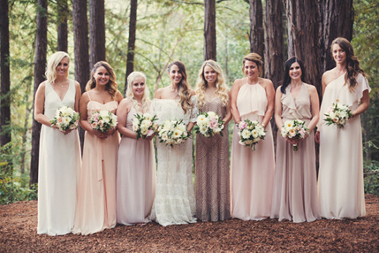 Bridesmaids in blush dresses hold bouquets in a forest setting