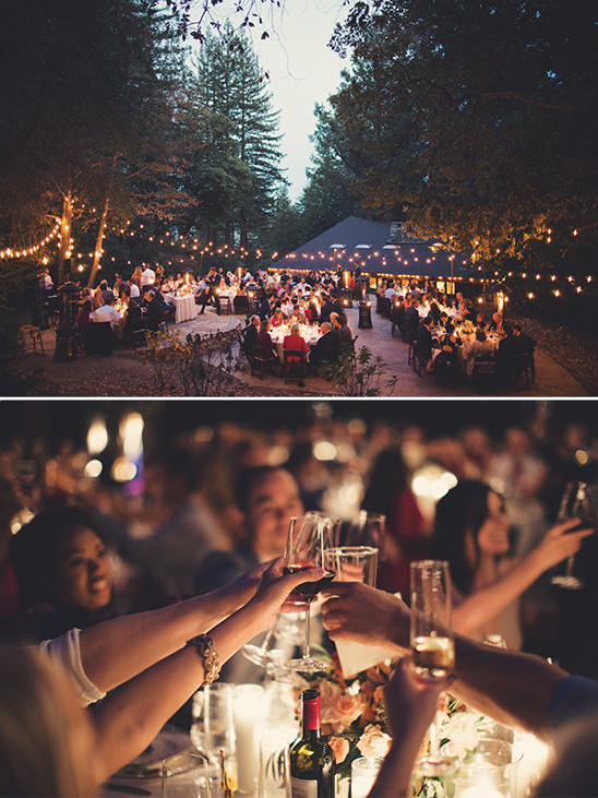 Outdoor wedding reception under string lights with guests toasting