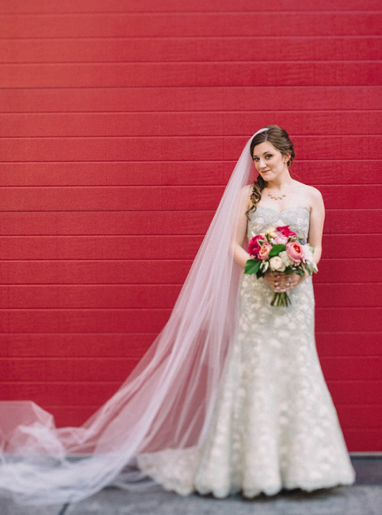 Elegant bride poses in her wedding dress against a red wall
