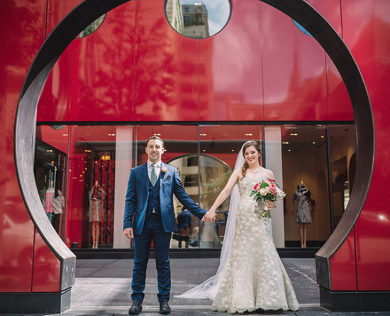 Newlyweds holding hands with vibrant red backdrop on their wedding day