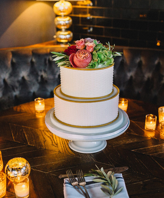 Two-tiered wedding cake with flower topping on a table with candles