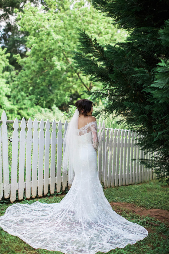 Bride in lace wedding dress veil back view white fence