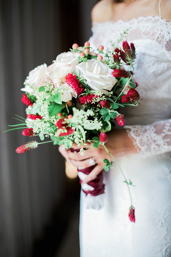 Lace dress bride holds romantic white and red rose bouquet