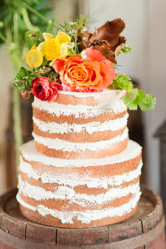 Naked wedding cake with flowers on rustic barrel stand