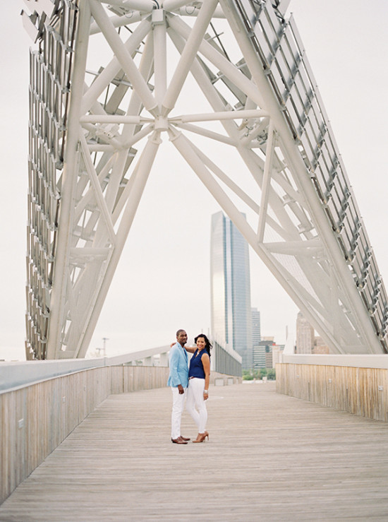 Couple poses on bridge with cityscape background