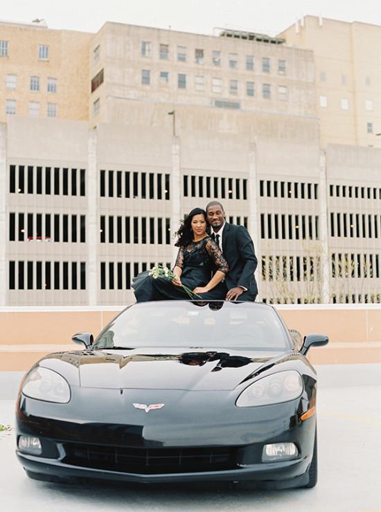 Elegant couple poses on a black Corvette sports car