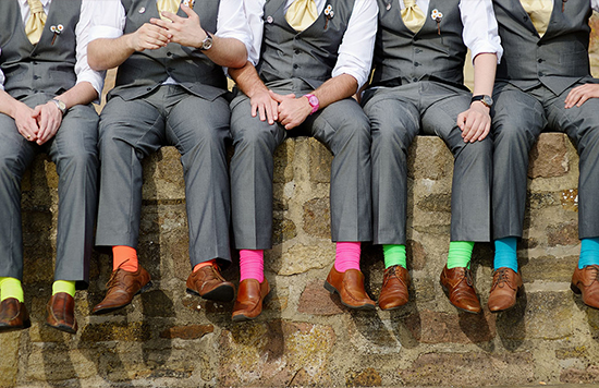 Groomsmen in suits showing off colorful socks on a wall
