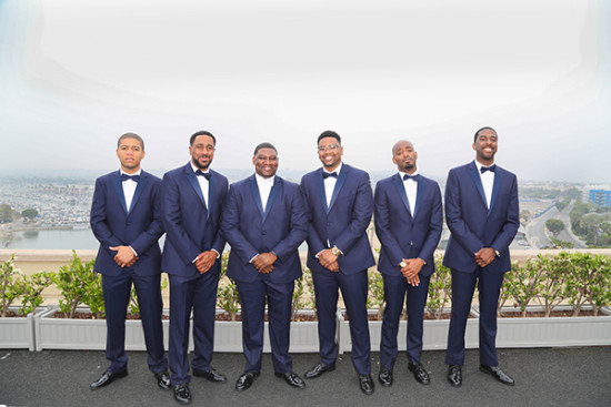 Groomsmen in navy tuxedos at an outdoor wedding venue