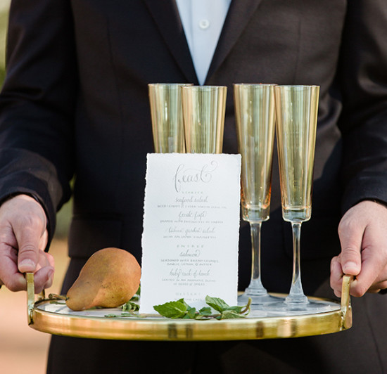 Waiter holding tray with glasses, menu, and pear