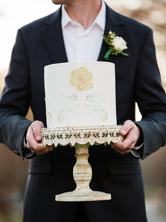 Groom holding a stylish wedding cake with floral design