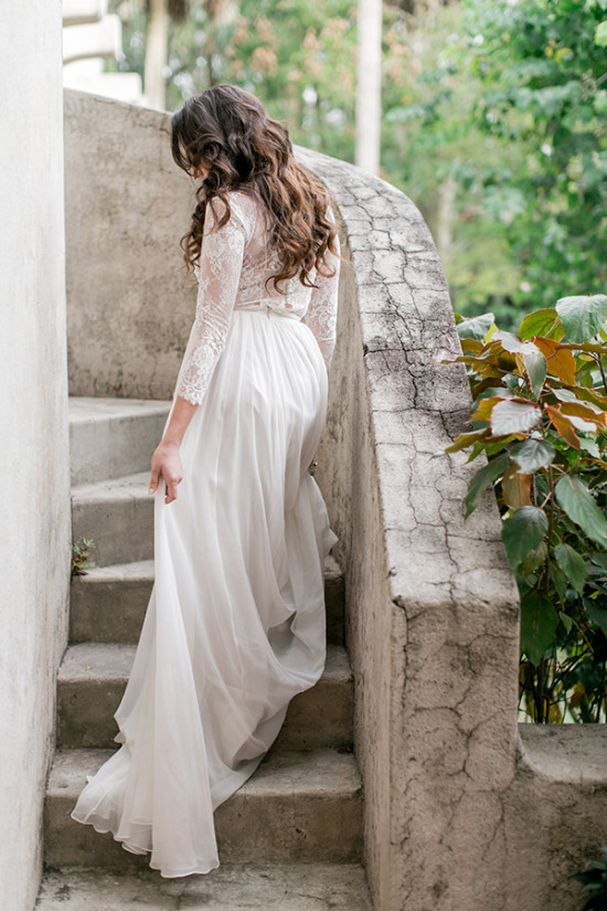 Bride in lace dress descends stone staircase outdoors