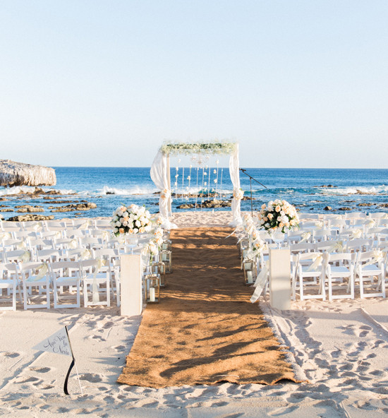 Beach wedding ceremony with white chairs and floral arch