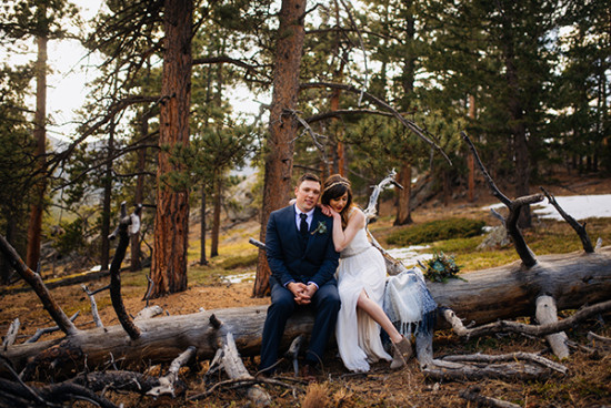 A happy couple sit on a log in forest wedding photo