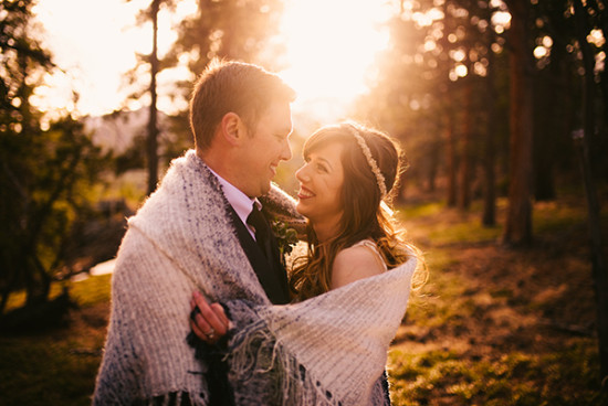Happy couple wrapped in blanket at sunset wedding
