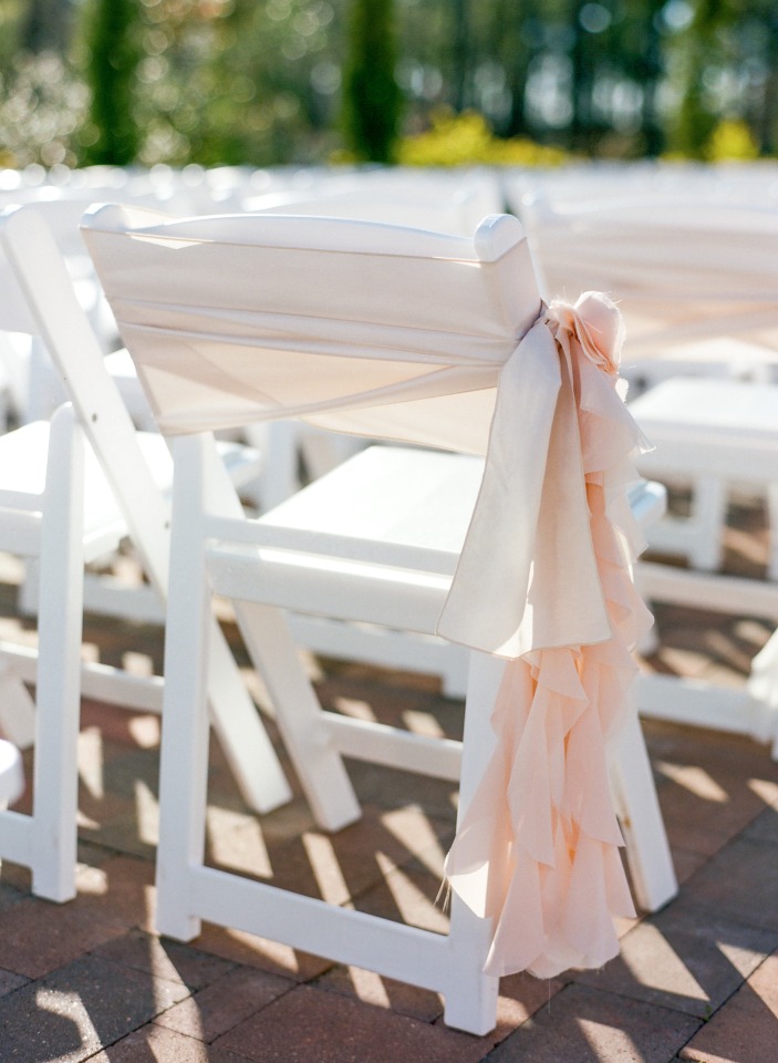White wedding chairs decorated with flowing peach fabric