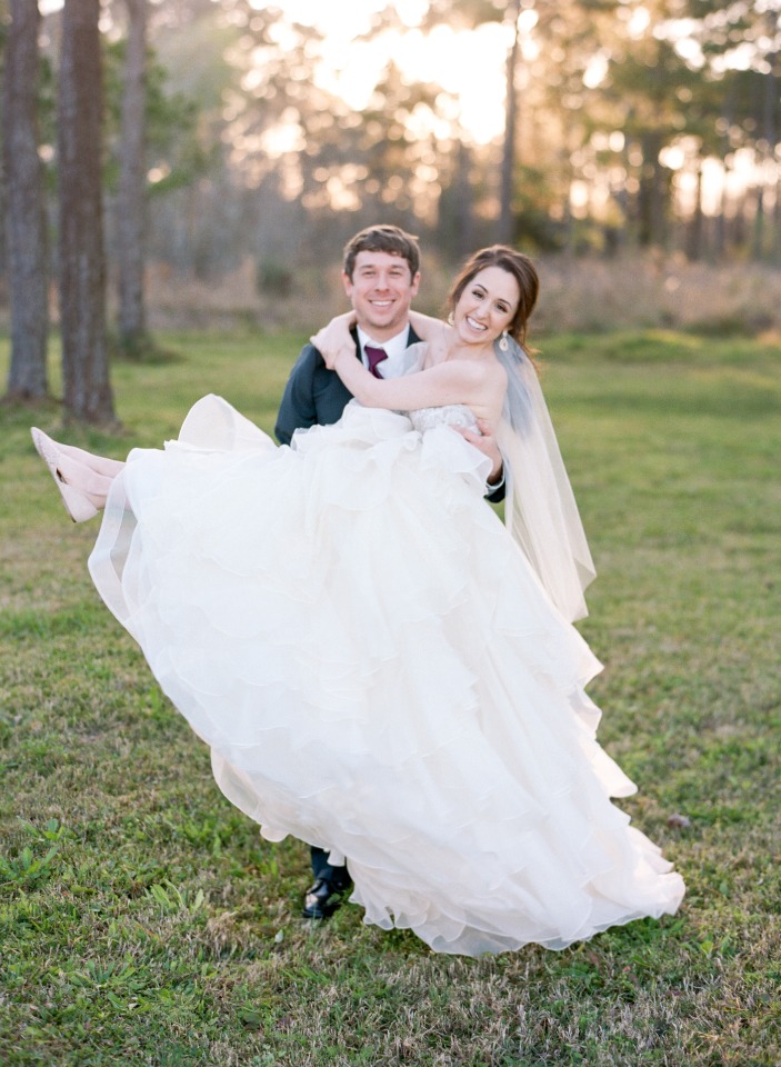Happy groom carries smiling bride in grassy field outdoors