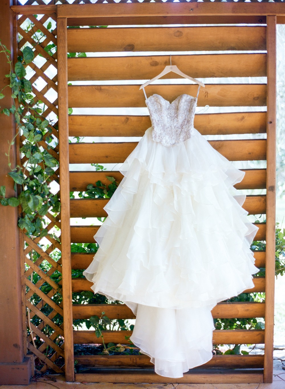 Ivory ruffled wedding dress hangs on wooden trellis
