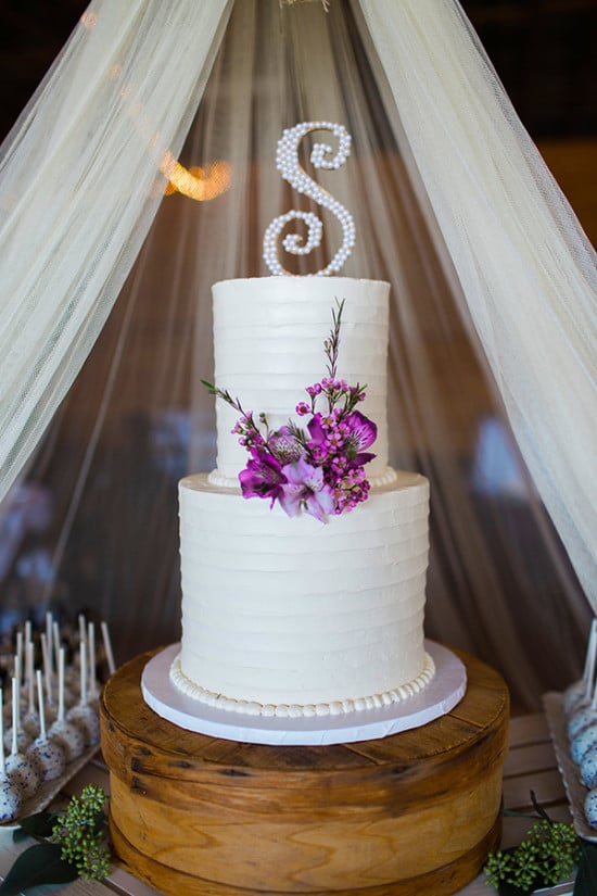 classic white wedding cake with purple flowers and initial topper