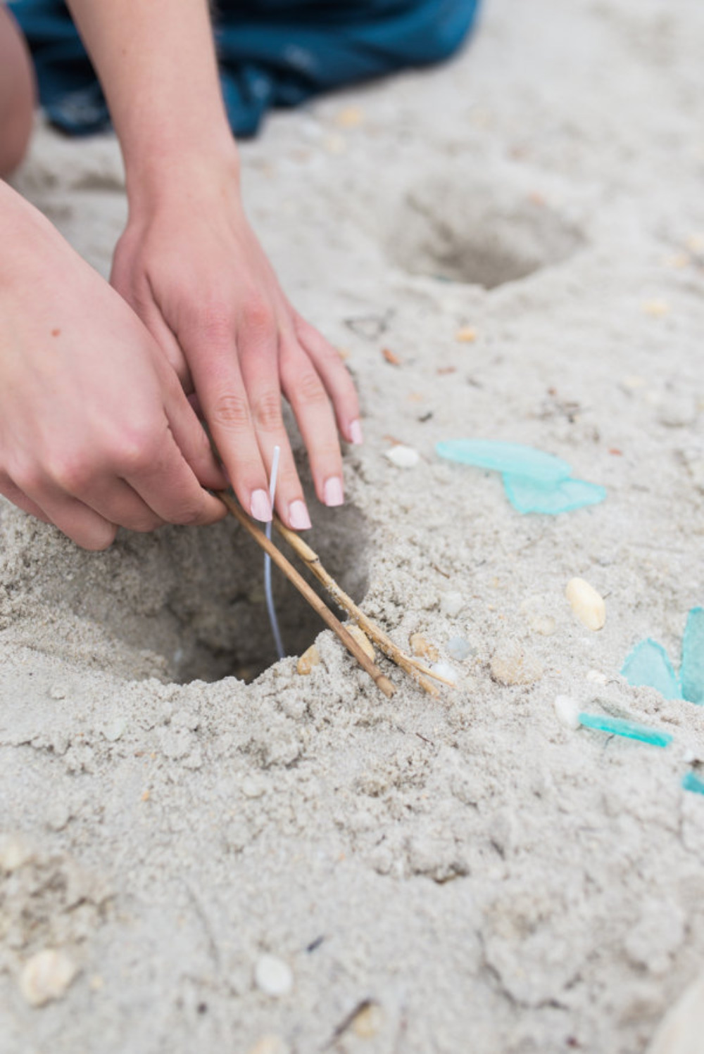 Hands dig hole in beach sand with sticks and shells