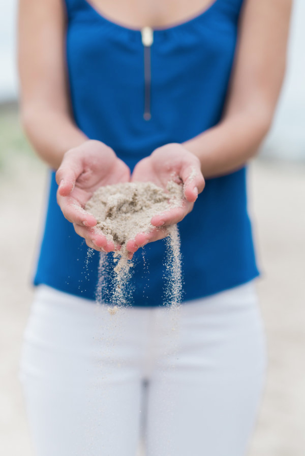 Woman in blue shirt holding sand, letting it fall through her hands