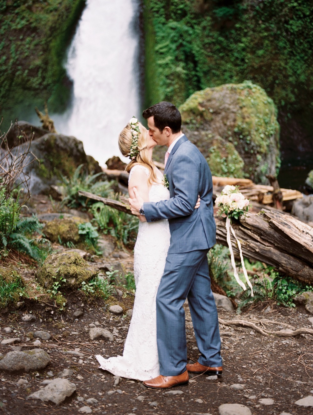 Wedding couple kissing before waterfall in Oregon forest