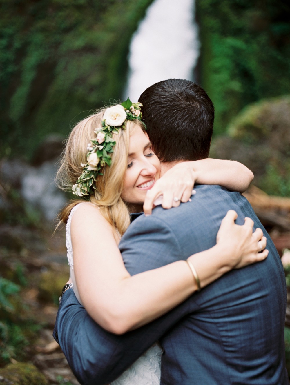 Bride and groom embrace near a waterfall on wedding day