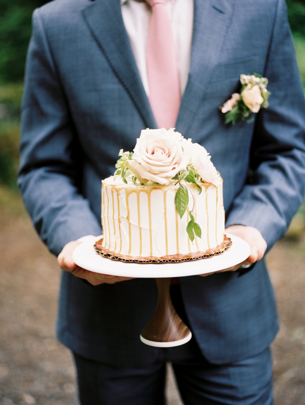 Groom holding elegant white wedding cake with roses