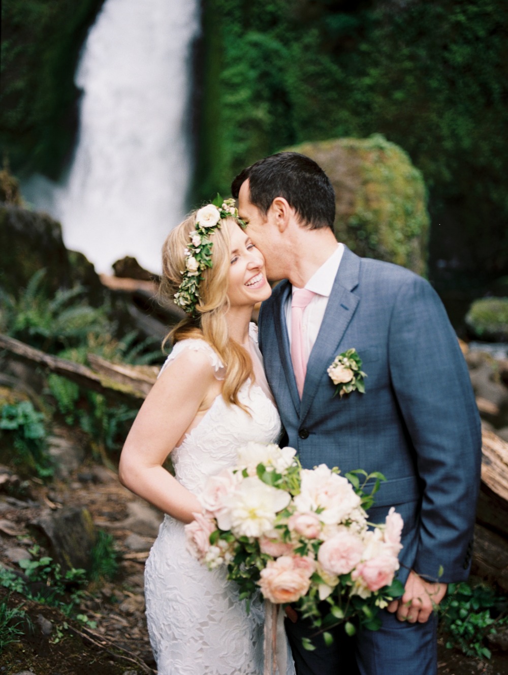 Happy bride and groom kiss near a waterfall